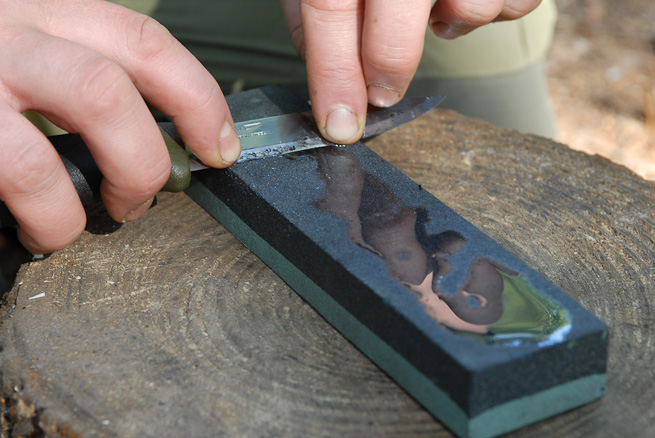 A man is sharpening a knife with sharpening stone