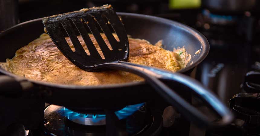 omelet & a spoon in an omelet pan on a burning stove