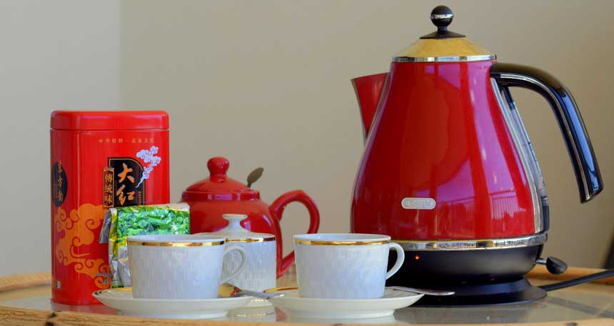 red colored gooseneck kettle along with white cups on a table