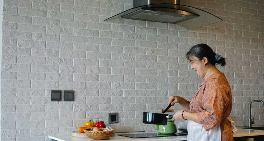 woman cooking something while a black range hood on top