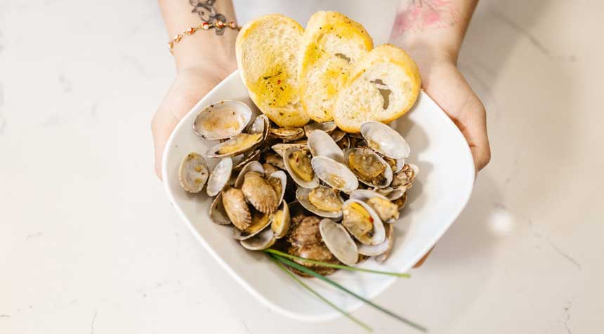 Girl holding a white bowl with clams & potatoes in it