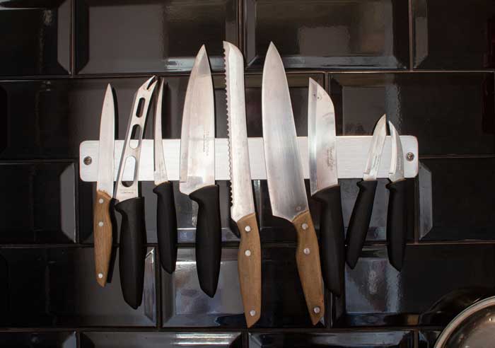 Different types of kitchen knives hanging by a wall on a stand
