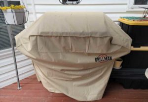 Beige colored Grillman grill cover in backyard covering a gas grill