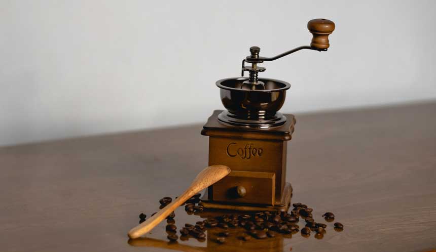 An old manual coffee grinder with coffee beans on wooden table