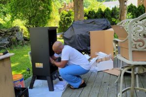 A man is assembling a propane smoker in backyard