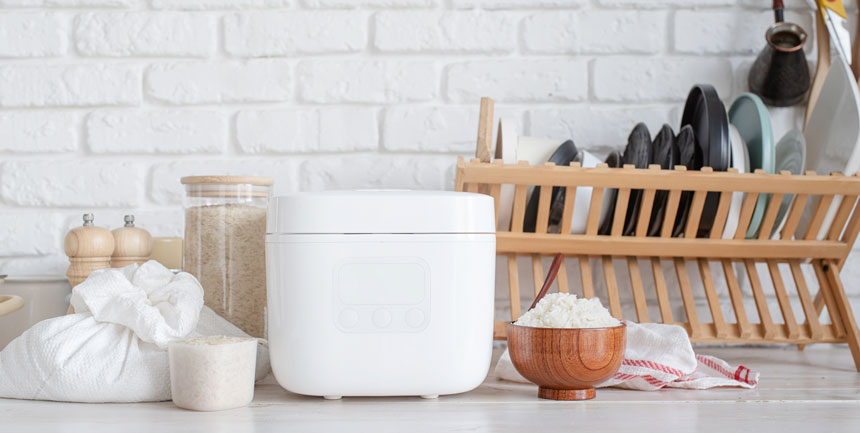 A white colored rice cooker on a kitchen shelf with other accessories around