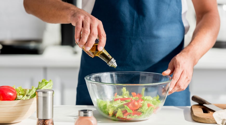 man pouring olive oil from an oil sprayer into a salad bowl
